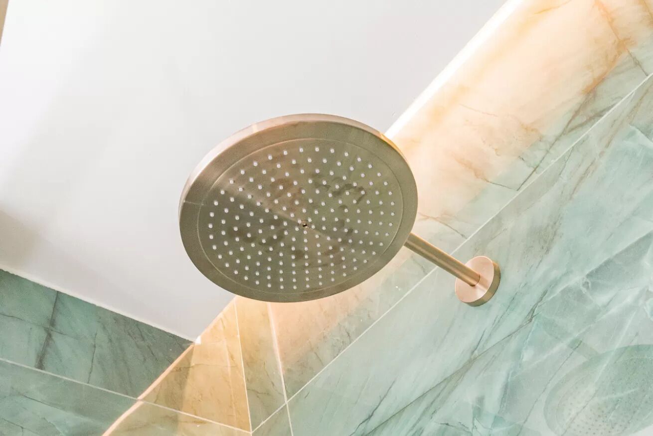 Un cabezal de ducha con diseño circular y acabado metálico, instalado en una pared con patrón de baldosas que imitan el mármol.
