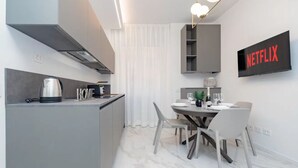 Ett modernt kök med en inbyggd spis, en vattenkokare och en kaffebryggare. Det finns en matplats med ett bord och stolar, och en tv som är monterad på väggen och visar "NETFLIX".
