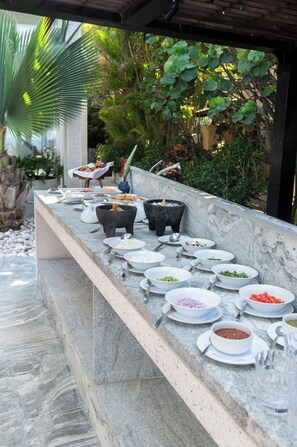 An outdoor buffet with various dishes and a stone mortar. - Breeze 5-18 | Oceanfront Villa | Infinity Pool (Cruz de Huanacaxtle)