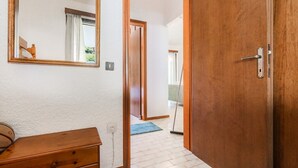 Een gang met een houten deur, een spiegel, een dressoir en een blauwe mat op de vloer.