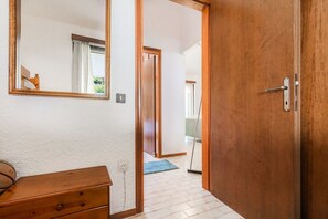 A hallway with a wooden door, a mirror, a dresser, and a blue mat on the floor. - Ieva Home by Rentals Pro - Elani Halkidiki (Elani)
