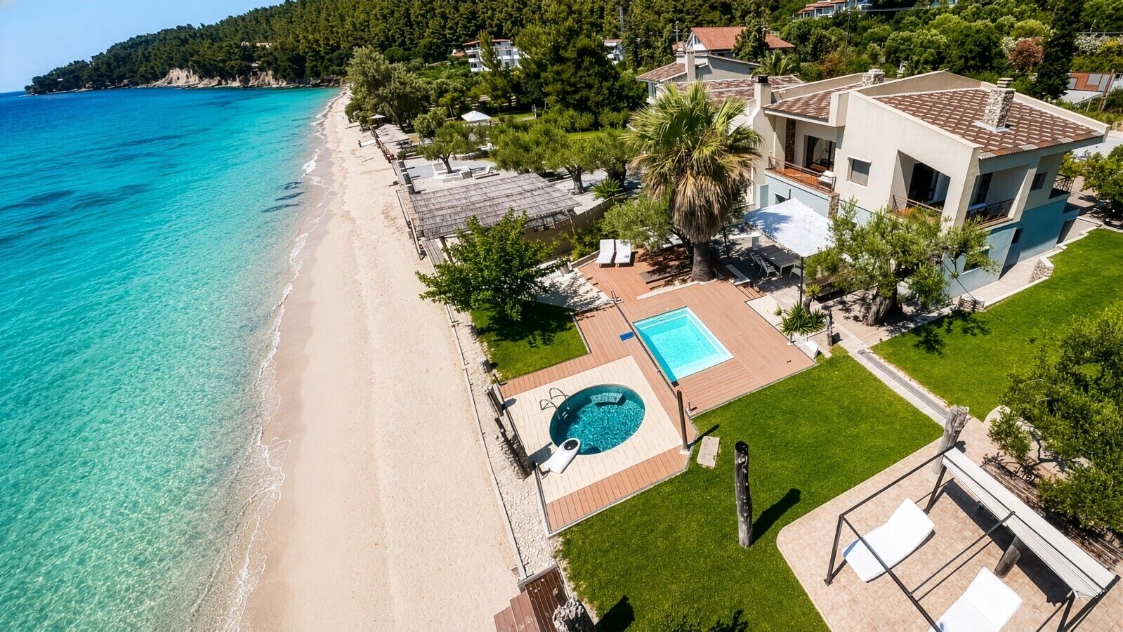 Vue aérienne d’une propriété située sur la côte, avec une plage, une piscine et une pelouse bien entretenue.
