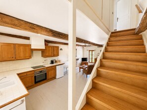 A kitchen with wooden cabinets, a dishwasher, and a dining area with a table and chairs. - At René's, sleeps 2, near Castelnaud Castle (Daglan)