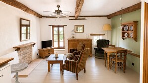 Una sala de estar acogedora con chimenea, televisor, mesa de comedor y ventilador de techo.