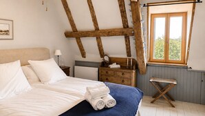 Un dormitorio con cama, mesita de noche, cómoda, ventana y estructura de vigas de madera en el techo.