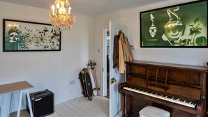 Una habitación con un piano, una araña, un monopatín y una puerta que da a otra estancia.
