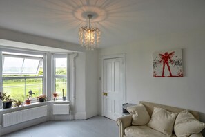 A room with a large window, a radiator, a beige sofa, and a chandelier.