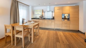 Eine moderne Küche mit Holzschränken, einem Esstisch mit Stühlen und einem großen Fenster mit Vorhängen.