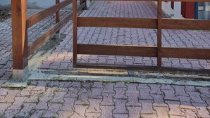 Un establo con cerca de madera, un edificio rojo y una zona pavimentada.