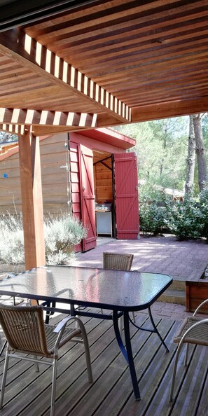 Eine überdachte Terrasse im Freien mit Tisch und Stühlen, ein rot gefärbtes, barnähnliches Gebäude und eine Holzterrasse.