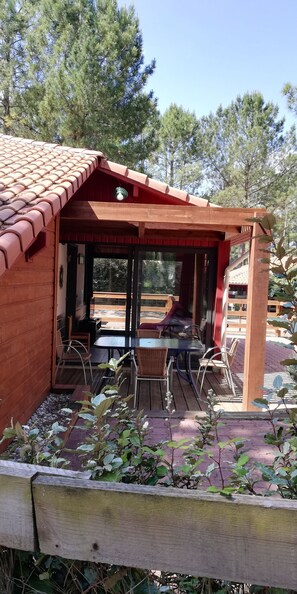 A wooden building with a tiled roof, a glass door entrance, and a patio area with tables and chairs. - House for 4 people in a complex with a pool (Moliets-et-Maa)