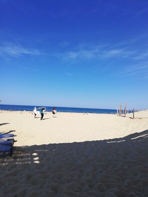 Ein Sandstrand mit blauem Himmel, wenigen Personen und einem Holzzaun.