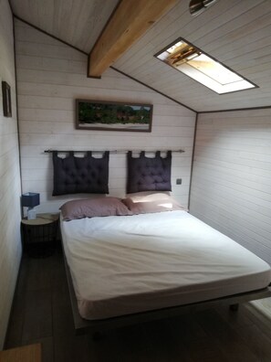 Ein kleines, gemütliches Schlafzimmer mit einem Einzelbett, einem Nachttisch, einem Wandregal und einem Dachfenster.