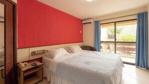 A hotel room with a bed, a desk with a telephone, a window with curtains, and a red accent wall. - Hotel Waikiki Beach Praia Azul (Natal)