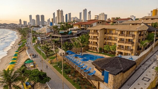 A coastal hotel with a pool, beachside seating, and a city skyline in the background. - Hotel Waikiki Beach Praia Azul (Natal)