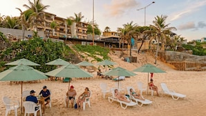 A beach with white lounge chairs and green umbrellas, palm trees, and buildings in the background. - Hotel Waikiki Beach Praia Azul (Natal)