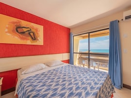 Una habitación de hotel con una cama, un ventanal con vistas a la playa y una pared roja con textura.