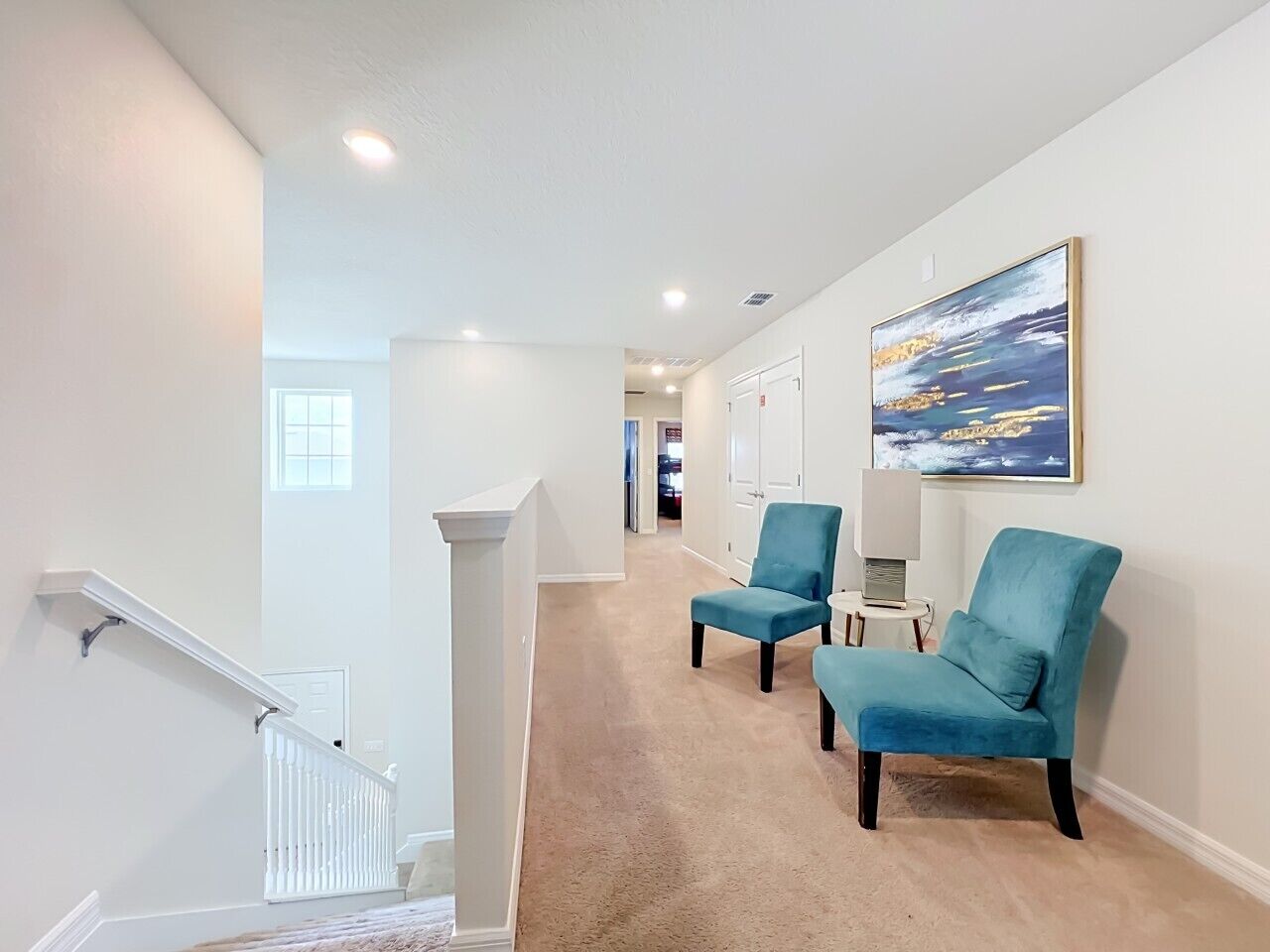 A hallway with a carpeted floor, a white staircase, and two blue armchairs.