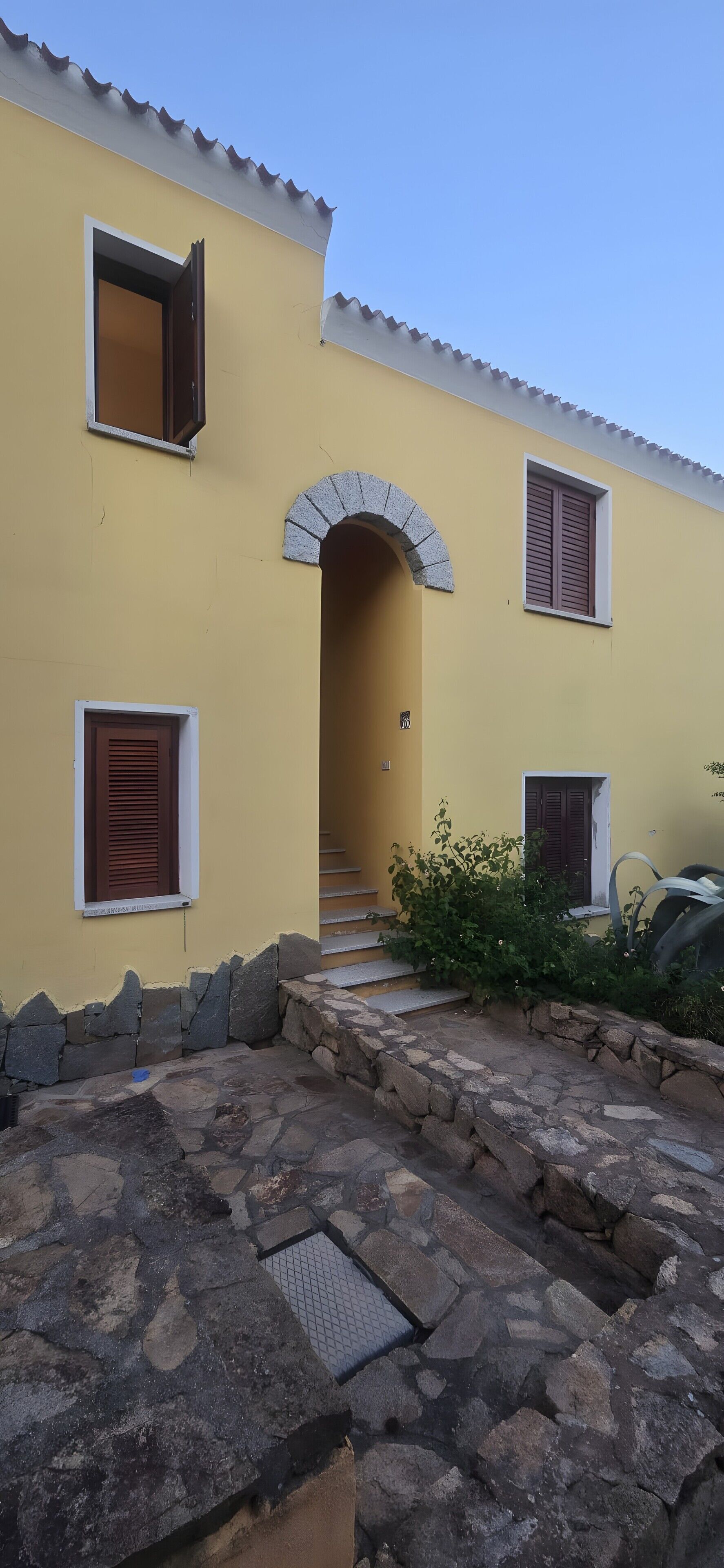 Un edificio amarillo con una escalera de piedra que conduce a un arco de entrada, paredes de piedra y un pequeño jardín.