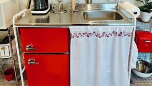 Pieni, käytännöllinen keittiö, jossa on kahvinkeitin, pesuallas ja punainen kaappi.