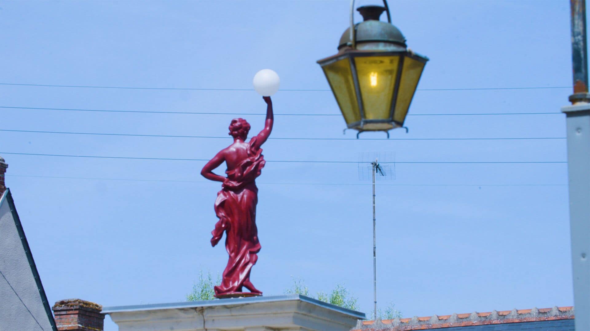 A statue of a woman on a pedestal with a street lamp above.