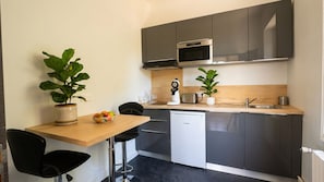 A compact kitchenette with a microwave, toaster, and sink. There is a small dining area with a table and chairs, and two potted plants.