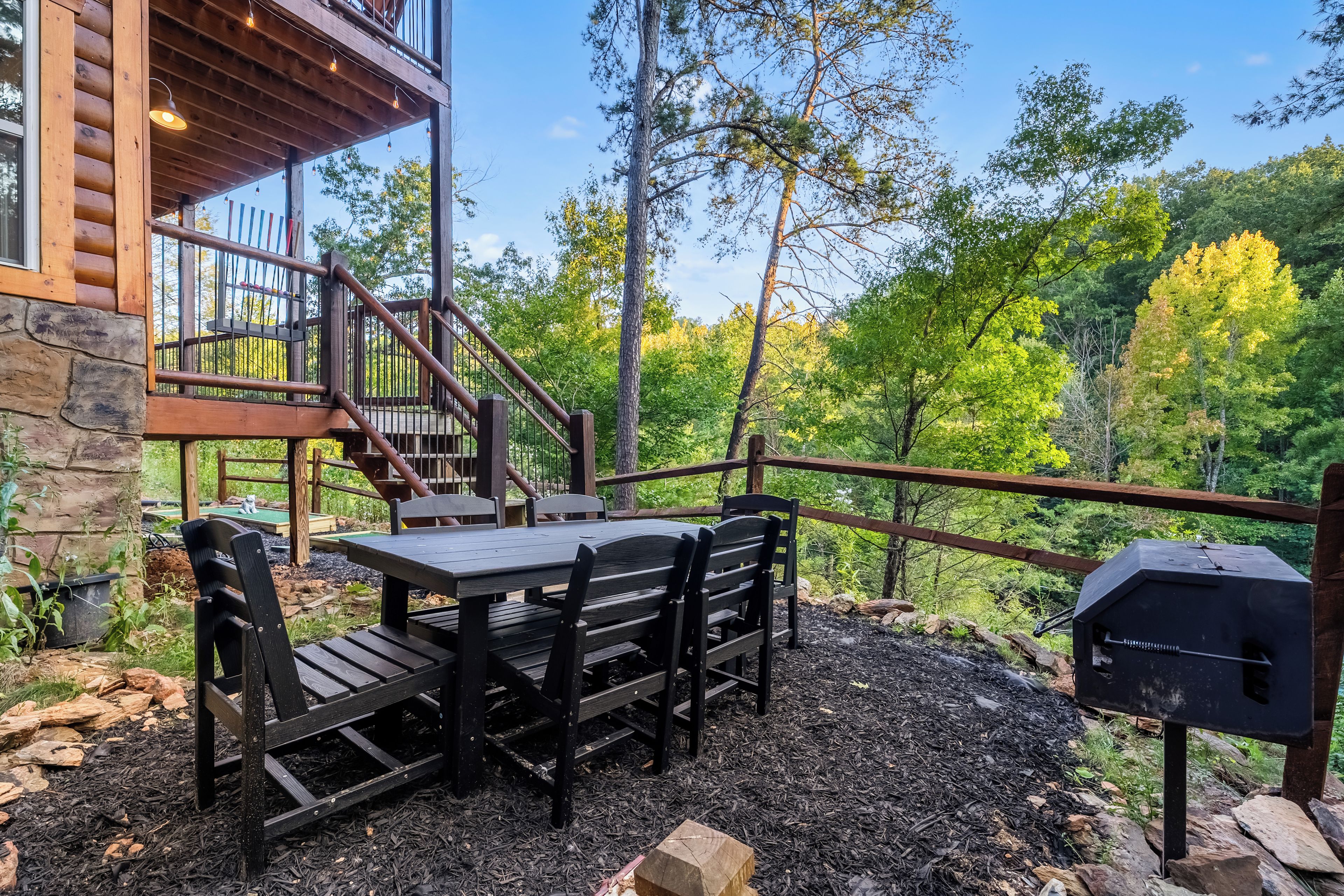 An outdoor patio with a table and chairs, surrounded by a wooden deck and a stone wall.