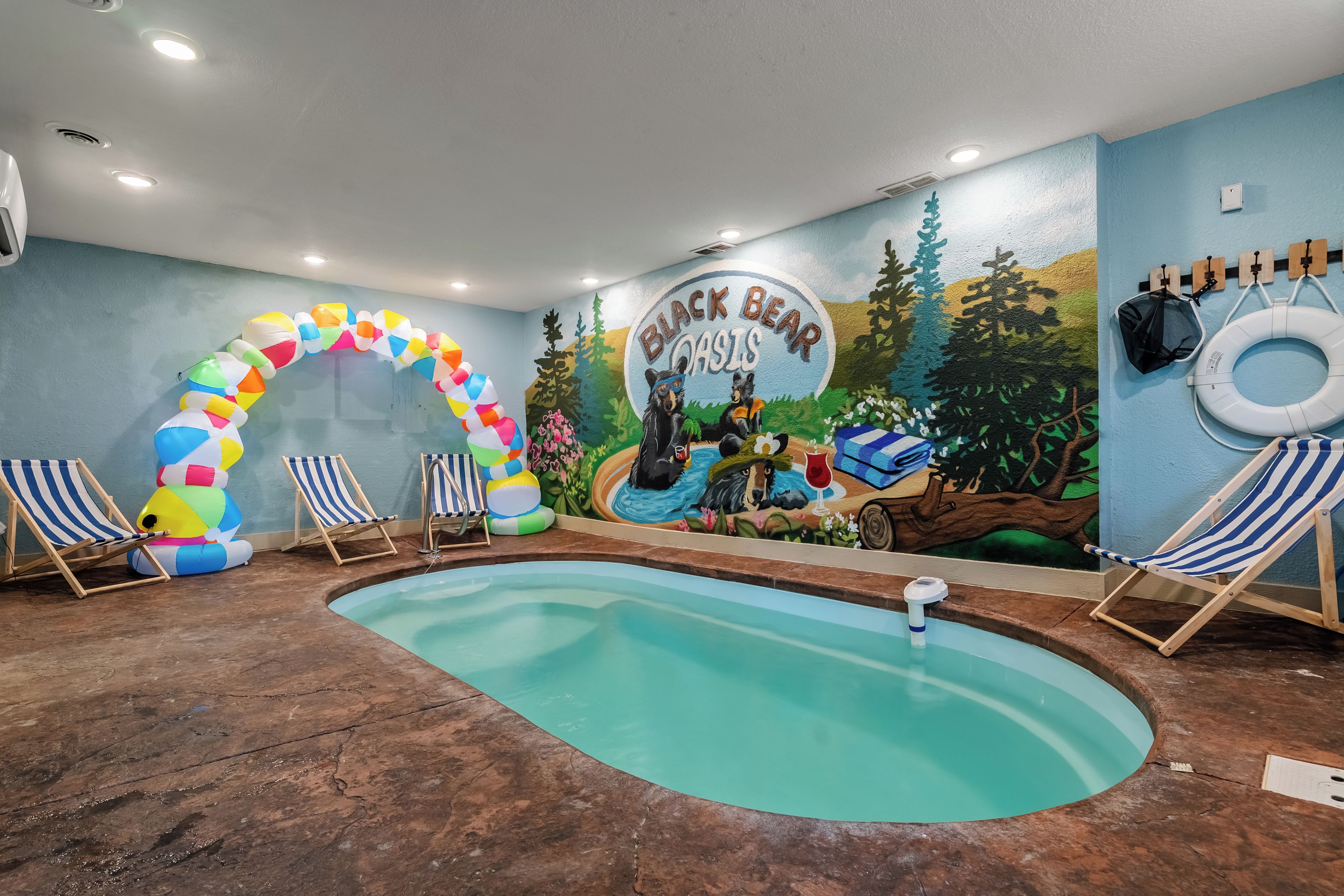 Un área de piscina con un mural, un arco inflable y sillones de descanso.
