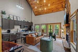 A spacious living area with a high ceiling, a fireplace, and a view of the outdoors. - 2 bed cabin w/ Indoor Pool & Gameroom (Sevierville)