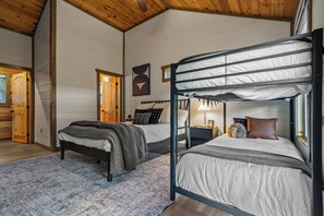 A room with two beds, wooden walls, a ceiling fan, and a small table with a lamp. - 2 bed cabin w/ Indoor Pool & Gameroom (Sevierville)