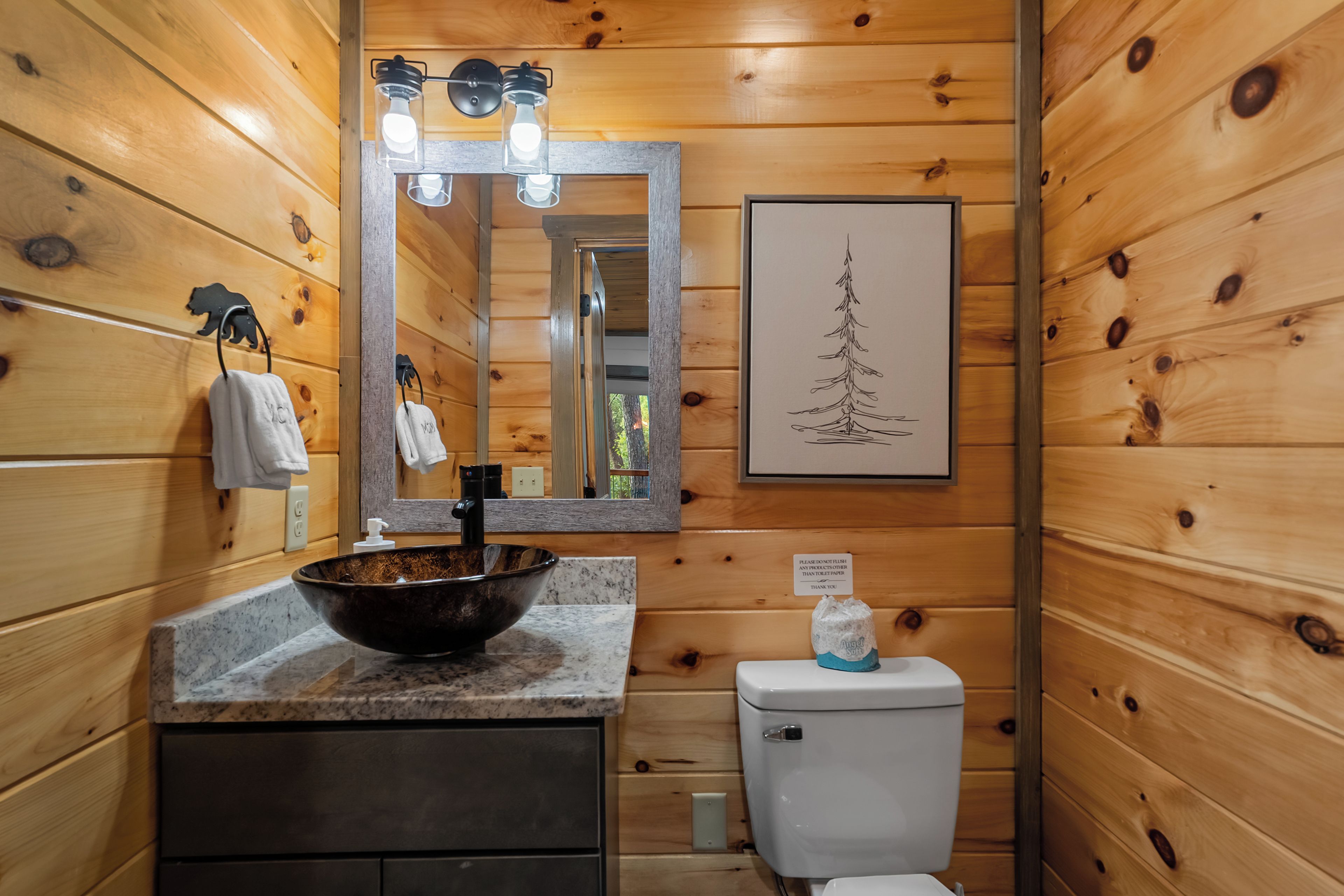 Ein Badezimmer in einer Holzhütte mit Waschbecken, Spiegel, Toilette und einem gerahmten Bild an der Wand.