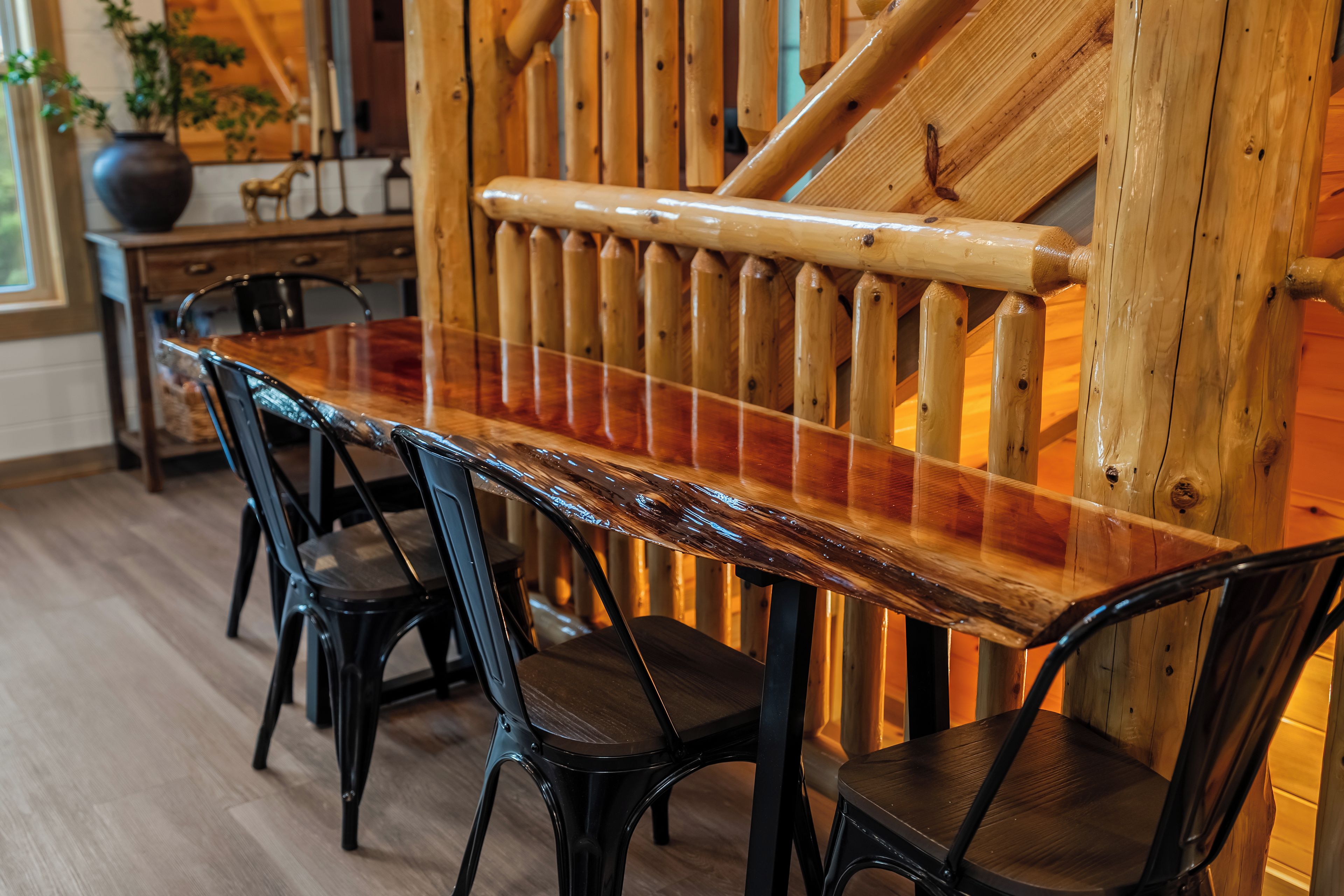 A wooden dining table with chairs, a staircase with wooden railings, and a vase with plants.