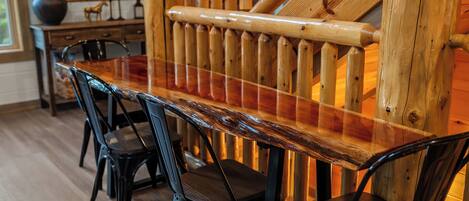 A wooden dining table with chairs, a staircase with wooden railings, and a vase with plants.