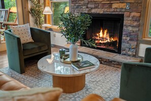 A cozy living room with a stone fireplace, a round coffee table with a vase and books, and comfortable seating. - 2 bed cabin w/ Indoor Pool & Gameroom (Sevierville)