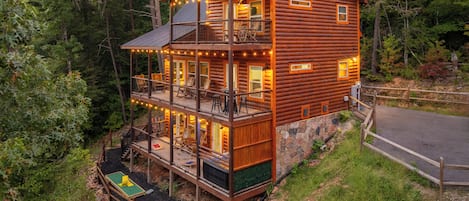 Una cabaña de troncos de varios pisos con balcón, mobiliario exterior y cimientos de piedra.