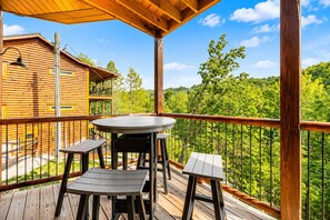 A wooden deck with a round table and two chairs, surrounded by a metal railing, overlooking a forested area. - 2 bed cabin w/ Indoor Pool & Gameroom (Sevierville)