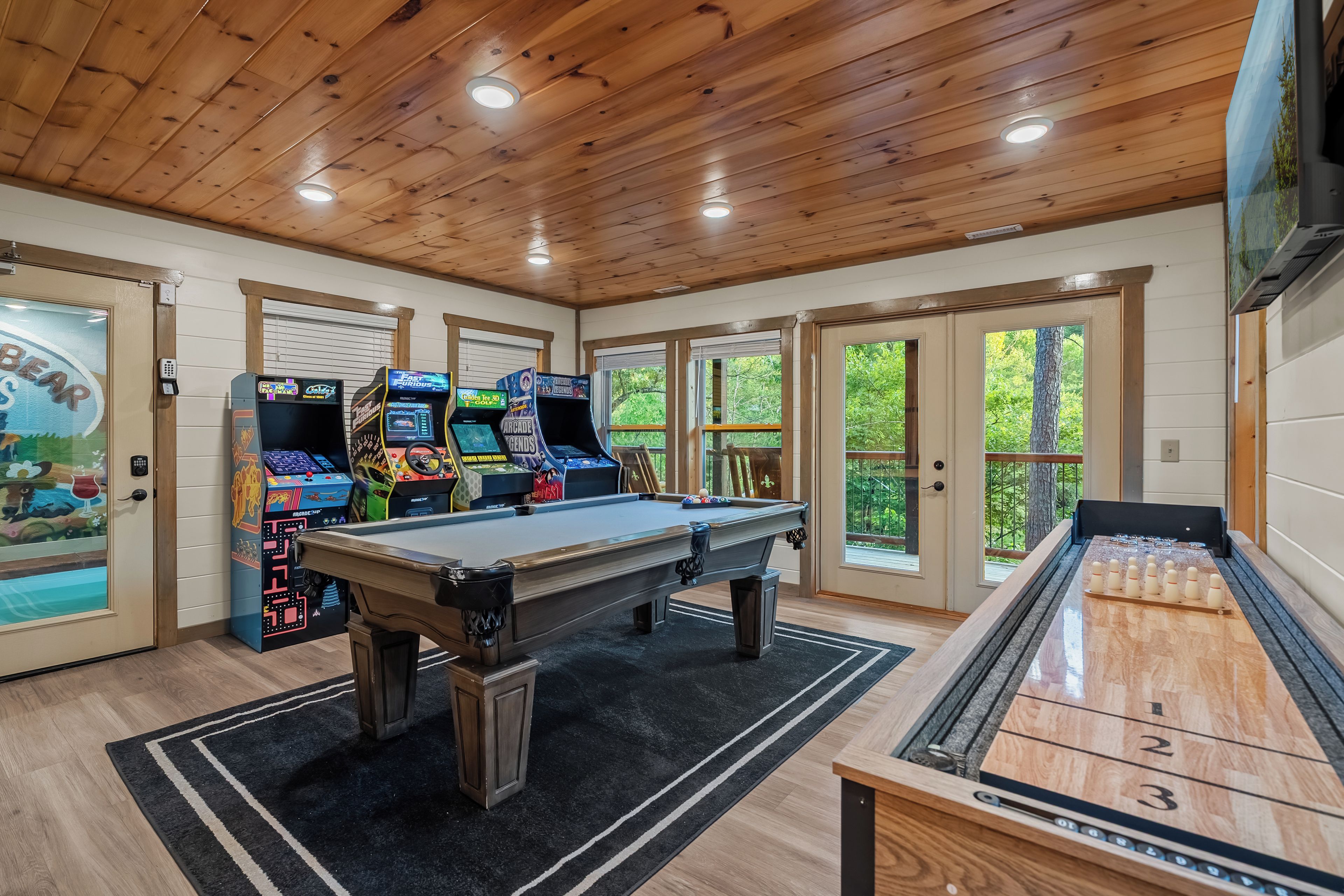 A room with a pool table, arcade games, and a shuffleboard table.