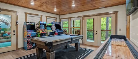 A room with a pool table, arcade games, and a shuffleboard table.