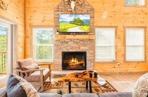 A cozy cabin interior with a stone fireplace, a television mounted above it, and a comfortable seating area with a coffee table. - 2 bed cabin w/ Indoor Pool & Gameroom (Sevierville)