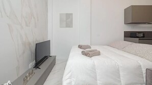 Ein modernes Hotelzimmer mit Flachbildfernseher, einem Bett mit weißer Bettwäsche, einer Wand mit Marmoroptik und minimalistischem Design.