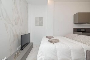 Ett modernt hotellrum med en platt-TV, en säng med vita sängkläder, en vägg med marmorliknande mönster och en minimalistisk design.
