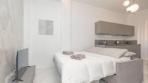 Ein modernes Schlafzimmer mit einem Bett, Nachttischen, einem Flachbildfernseher und einer integrierten Küchenzeile.