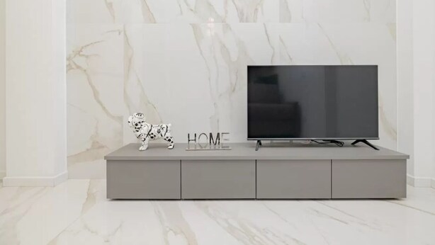 Ein modernes Wohnzimmer mit Marmorwand, einer grauen Unterhaltungsanlage, einem Flachbildfernseher und einer Dalmatinerfigur.