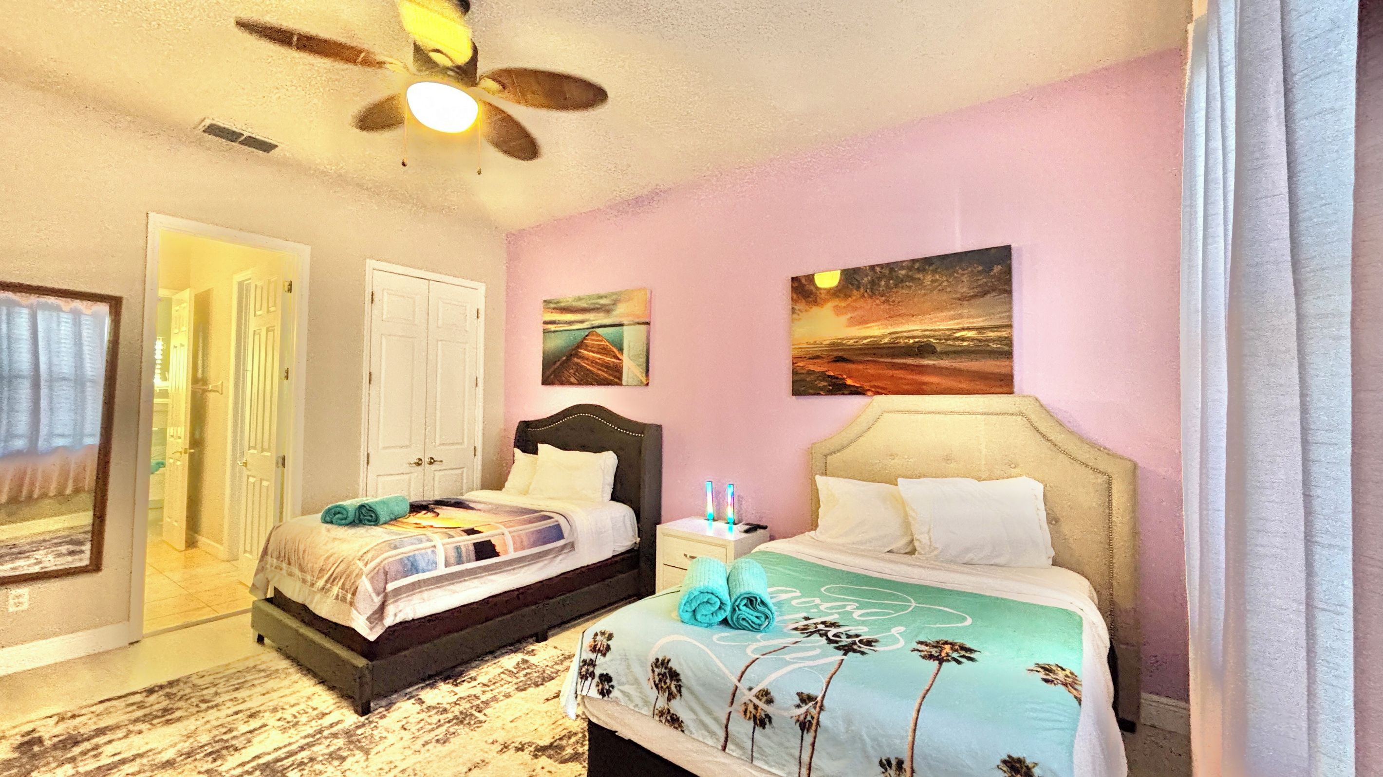A bedroom with two beds, a ceiling fan, and artwork on the walls.