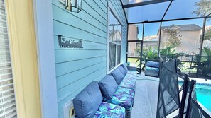 A covered outdoor seating area with a pool view, a sign reading 'Pool Towel,' and a screened porch. - Family Retreat for 14 in Reunion Resort with Pool (Kissimmee)