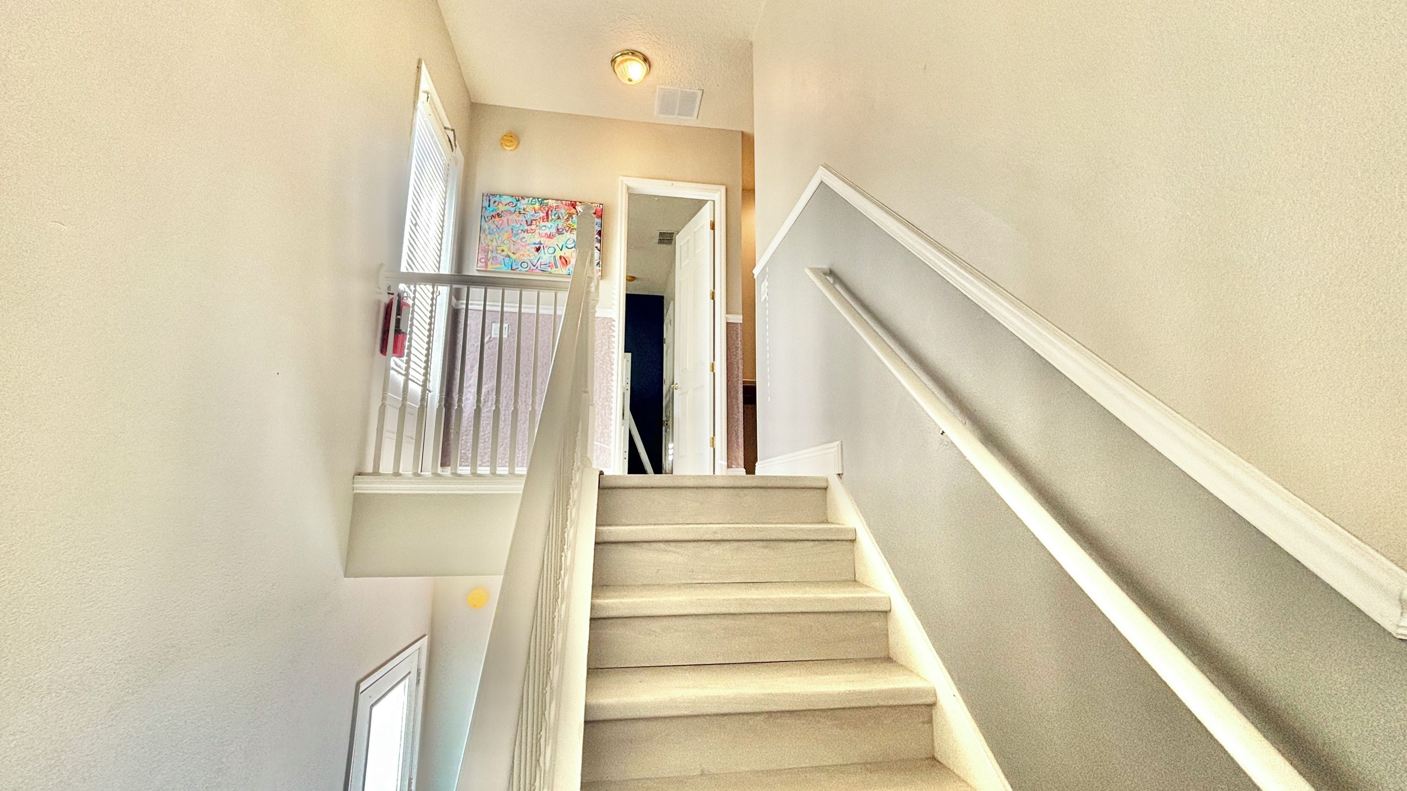A carpeted staircase with a handrail, leading to a room with a door and a window.