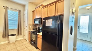 A compact kitchen with wooden cabinets, a black refrigerator, a microwave, and a stove. - Family Retreat for 14 in Reunion Resort with Pool (Kissimmee)