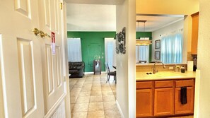 A hallway leading to a living room with a green accent wall, a dining area with a chair and table, and a kitchen with wooden cabinets and a sink. - Family Retreat for 14 in Reunion Resort with Pool (Kissimmee)