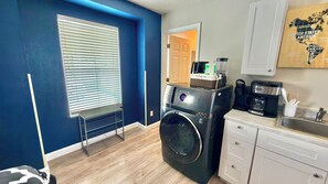 A laundry area with a front-loading washer and dryer, a coffee maker, and a sink with a countertop. - Private Renovated Queen Studio with W/D (Kissimmee)