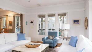 Un salón con un sofá blanco, un sillón azul, una mesa de centro y vistas al exterior a través de amplios ventanales.